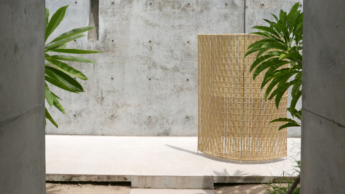 Modern minimalist concrete courtyard with tropical plants and a tall woven wicker basket in the center.