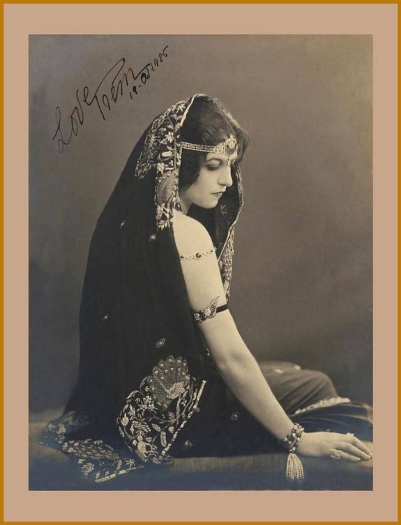 Vintage portrait of a seated woman in ornate attire and headdress from the early 20th century, facing sideways.