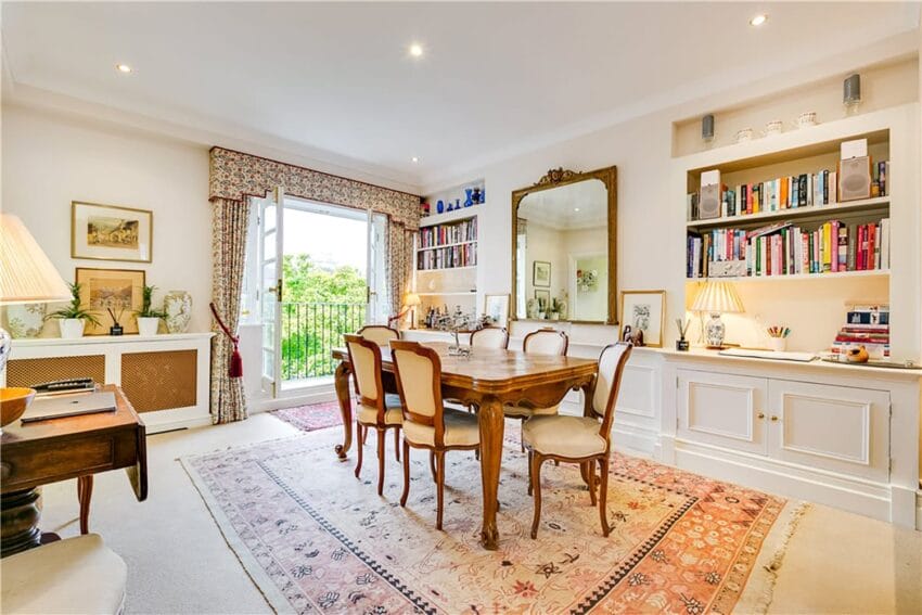 Elegant dining room with wooden table, vintage chairs, bookshelves, large mirror, and door opening to garden view.