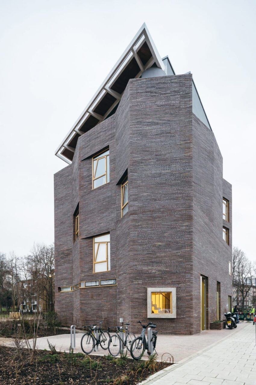 Modern angular brick building with bicycles parked outside, featuring large windows and a unique architectural design.
