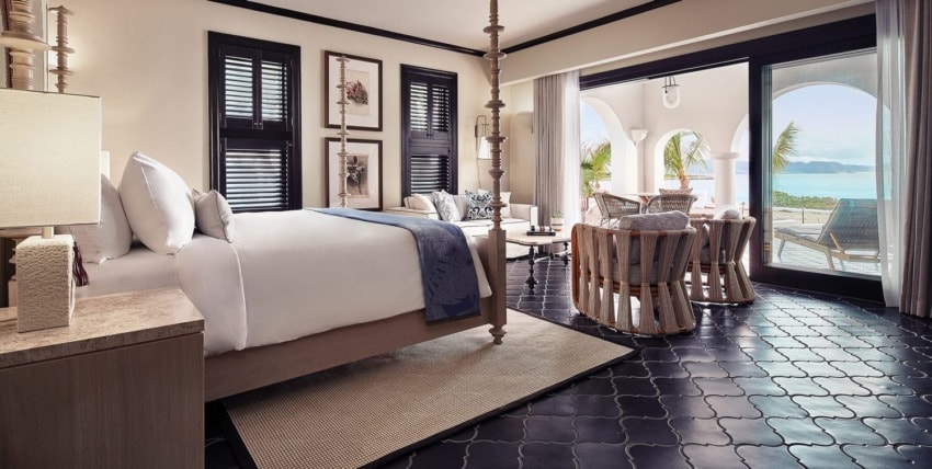 Luxury hotel room with ocean view, elegant furnishings, large bed, seating area, and arched windows leading to a balcony.