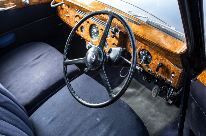 Vintage car interior with a wooden dashboard, black steering wheel, and blue seats.