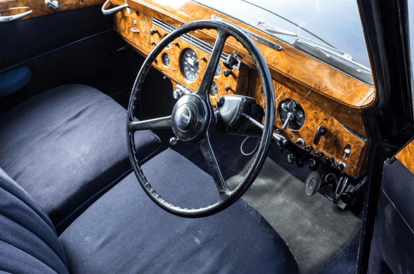 Vintage car interior with a wooden dashboard, black steering wheel, and blue seats.