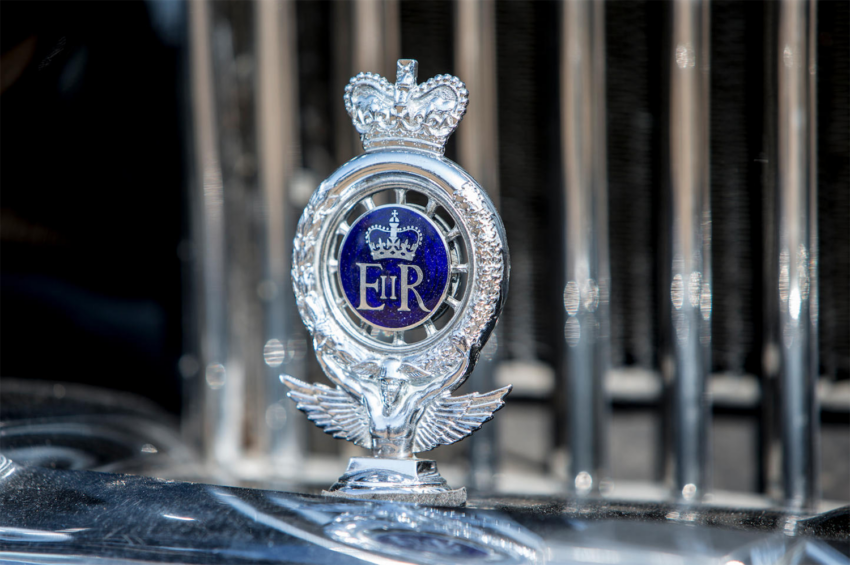 Royal emblem with crown and wings on a vintage car grille.