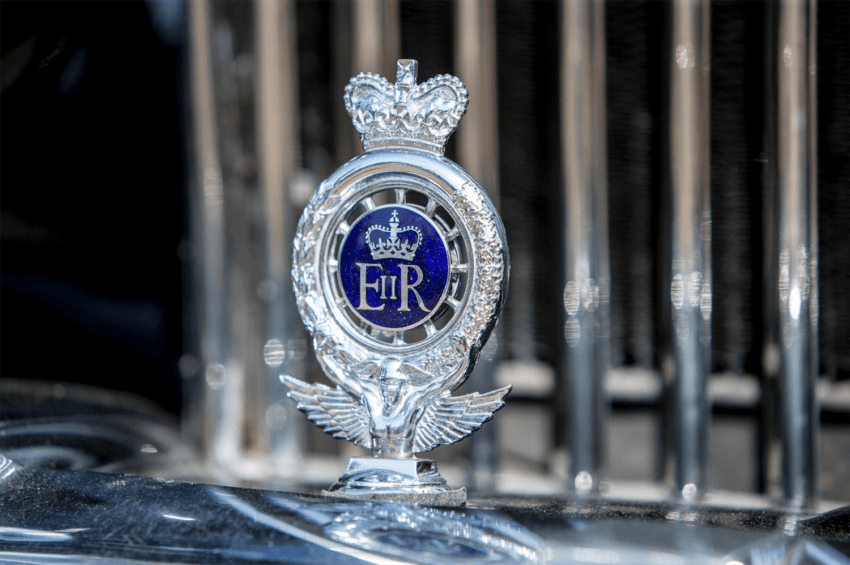Royal emblem with crown and wings on a vintage car grille.