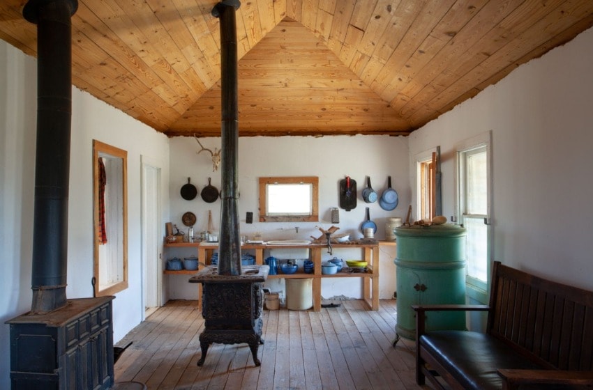 Rustic kitchen interior with wooden ceiling, vintage stove, cabinets, and cookware on shelves.