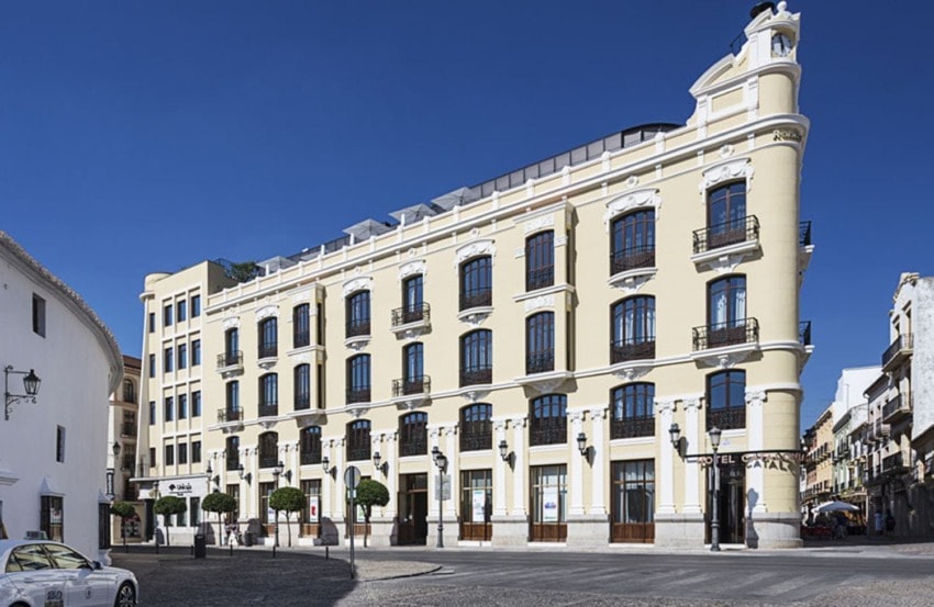 Elegant historic building with balconies and arched windows under a clear blue sky, located in a European square.