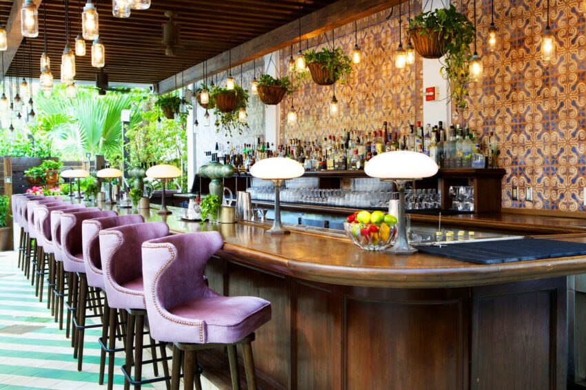 Elegant bar with purple stools, ornate tile walls, and hanging plants, creating a cozy and inviting atmosphere.