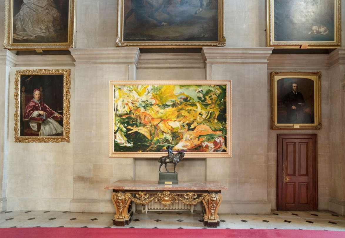 Gallery room with a large colorful abstract painting, ornate table, and several portraits on a stone wall.