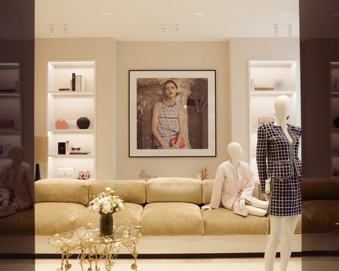 Fashionable boutique interior with a stylish mannequin, beige sofa, wall art, and elegant decor items on shelves.