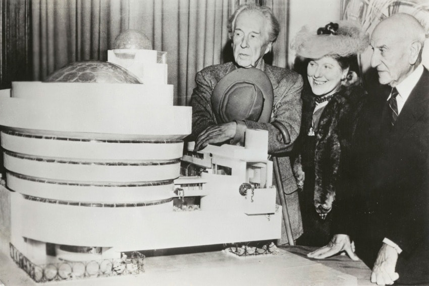 Architects and patrons examining Guggenheim Museum model, featuring spiraling ramps and a domed roof in a historical setting.