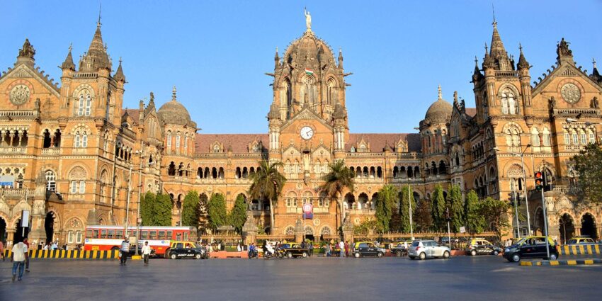 Facade of the historic Chhatrapati Shivaji Terminus in Mumbai with bustling street and vehicles in the foreground.