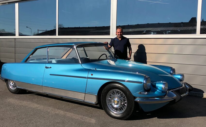 man standing beside a vintage blue car parked in front of a building