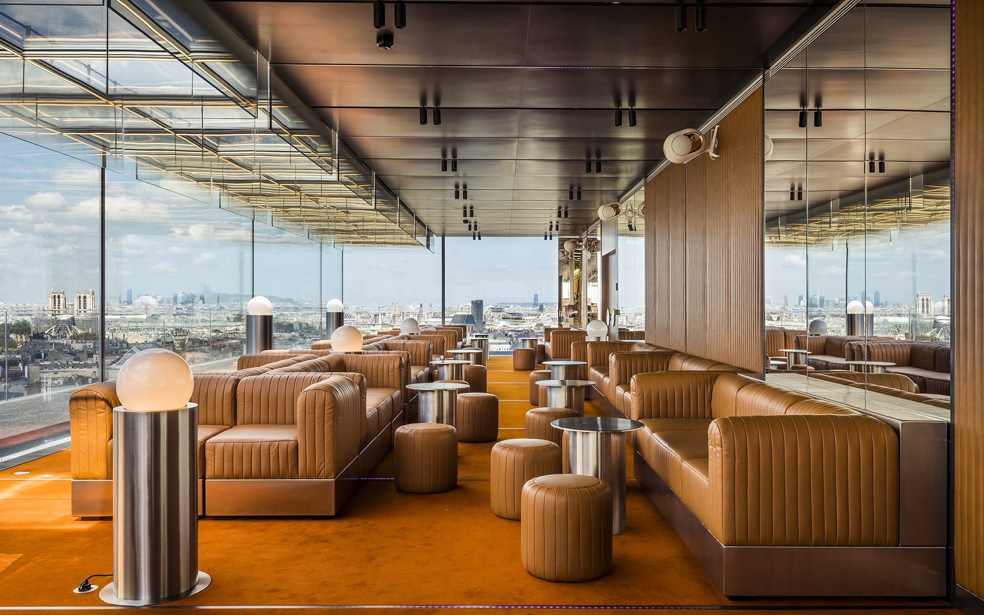 Modern rooftop lounge with brown leather seating, panoramic city views, and industrial lighting against a clear sky backdrop.