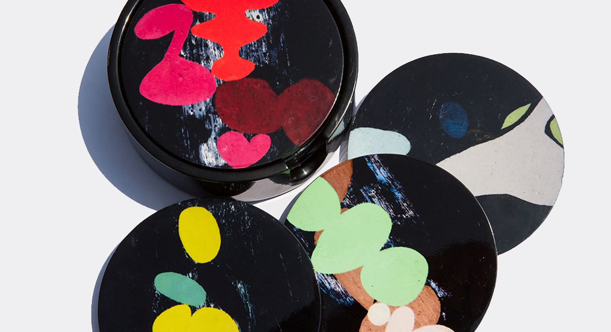 Four round coasters with abstract colorful designs on a light background.