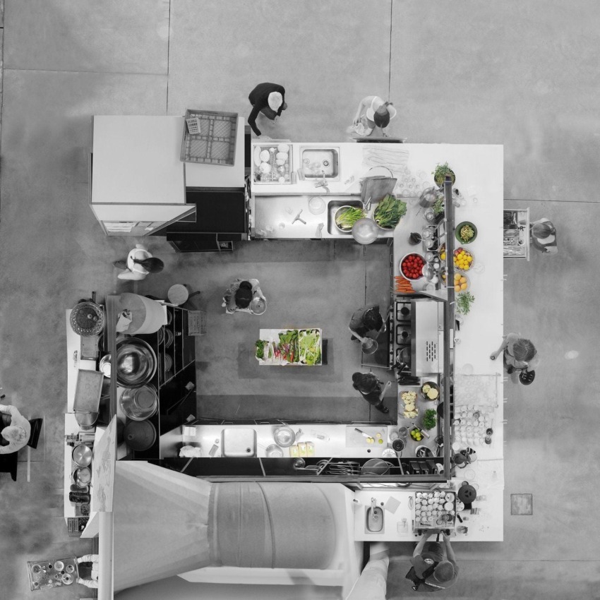 Top view of a bustling professional kitchen with chefs preparing various dishes, featuring fresh vegetables and ingredients.