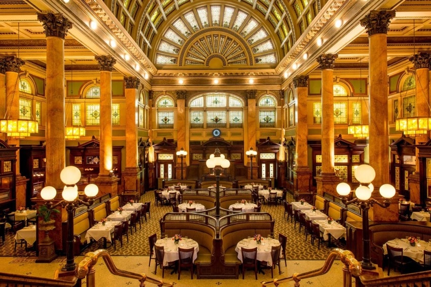 Grand ornate dining hall with arched ceiling, elegant lighting, and intricately designed seating areas.