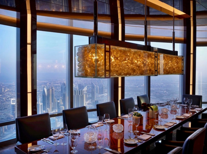 Luxurious dining room with elegant table setting, modern chandelier, and panoramic cityscape view through large windows.