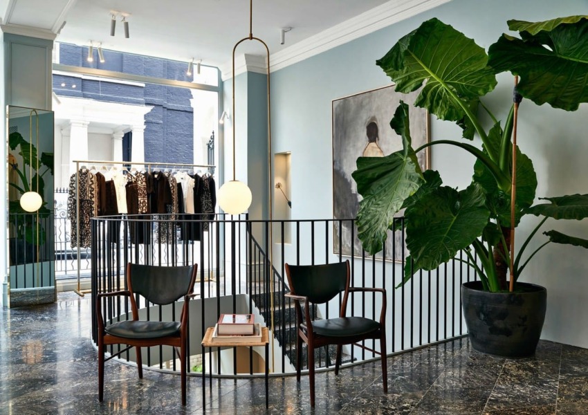 Stylish boutique interior with chairs, large plant, round mirror, hanging clothes, and modern lighting on marble floor.