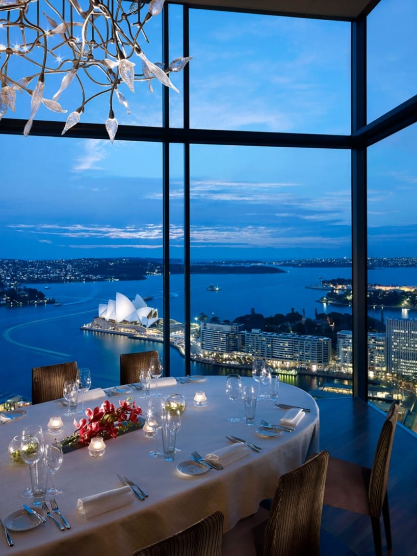 Elegant dining setup with a stunning view of a city skyline and iconic opera house at dusk.