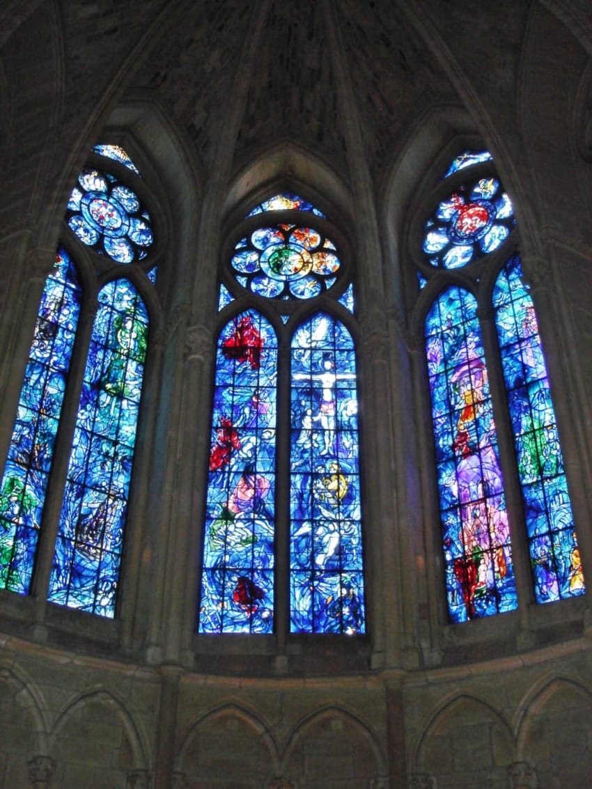 Stained glass windows with vibrant blues and reds in a cathedral setting, depicting intricate designs and religious scenes.