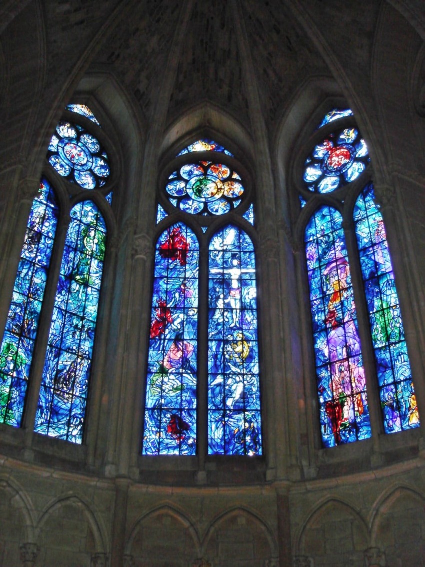 Stained glass windows with vibrant blues and reds in a cathedral setting, depicting intricate designs and religious scenes.