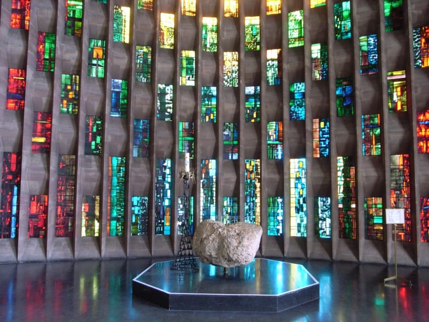 Colorful stained glass windows in a modern church interior with a large stone altar in the center.
