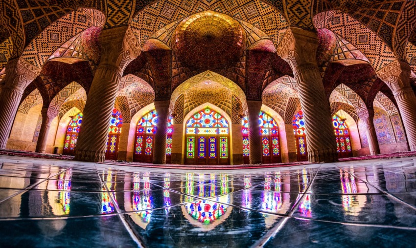 Vibrant stained glass windows and intricate tile patterns inside a grand mosque, reflecting on a polished floor.