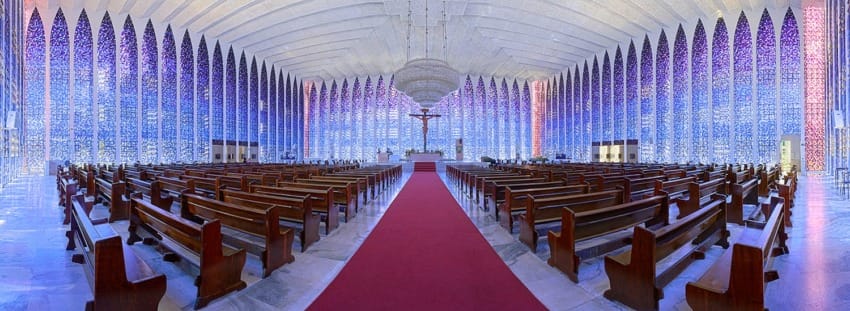 Interior view of a cathedral with colorful stained glass windows and rows of wooden pews leading to the altar.