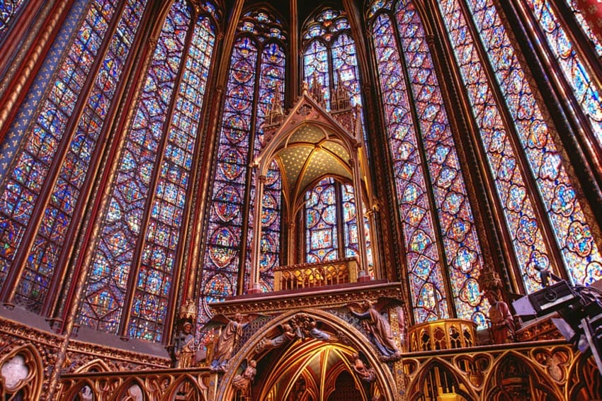 Interior of Sainte-Chapelle with ornate stained glass windows and Gothic architectural details in vibrant colors.