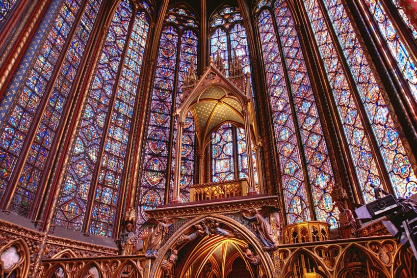 Interior of Sainte-Chapelle with ornate stained glass windows and Gothic architectural details in vibrant colors.