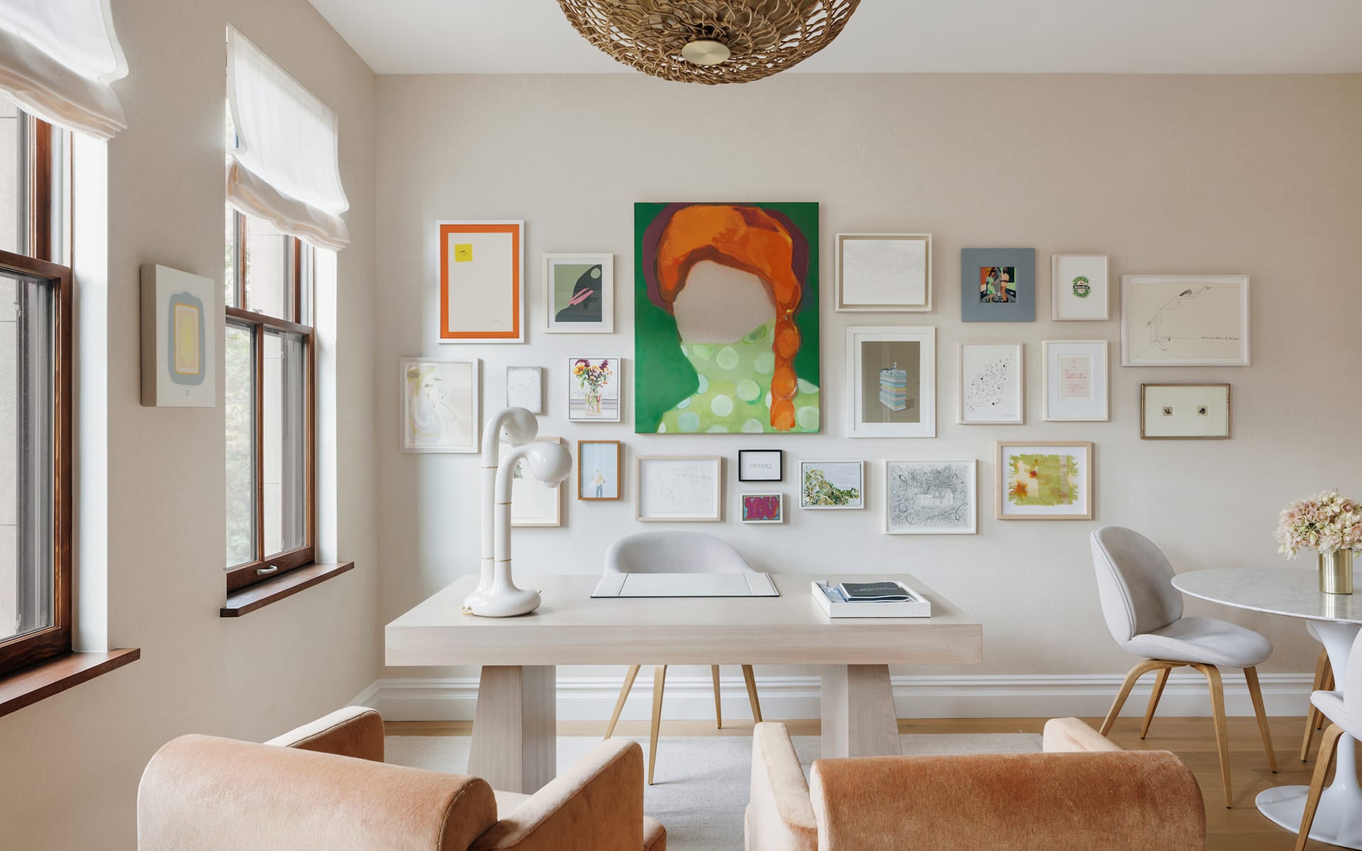 Bright, modern home office with gallery wall, light wooden desk, two brown chairs, and white round table with chairs.