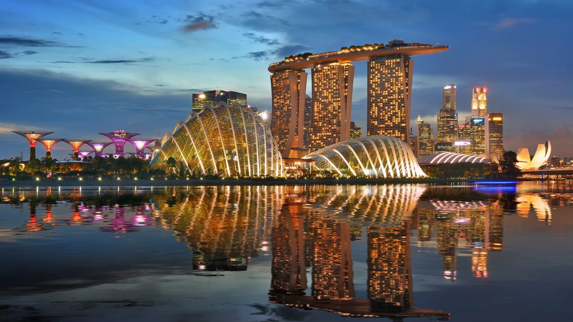 Singapore skyline at dusk with iconic Marina Bay Sands, Supertree Grove, and city lights reflecting on the water.