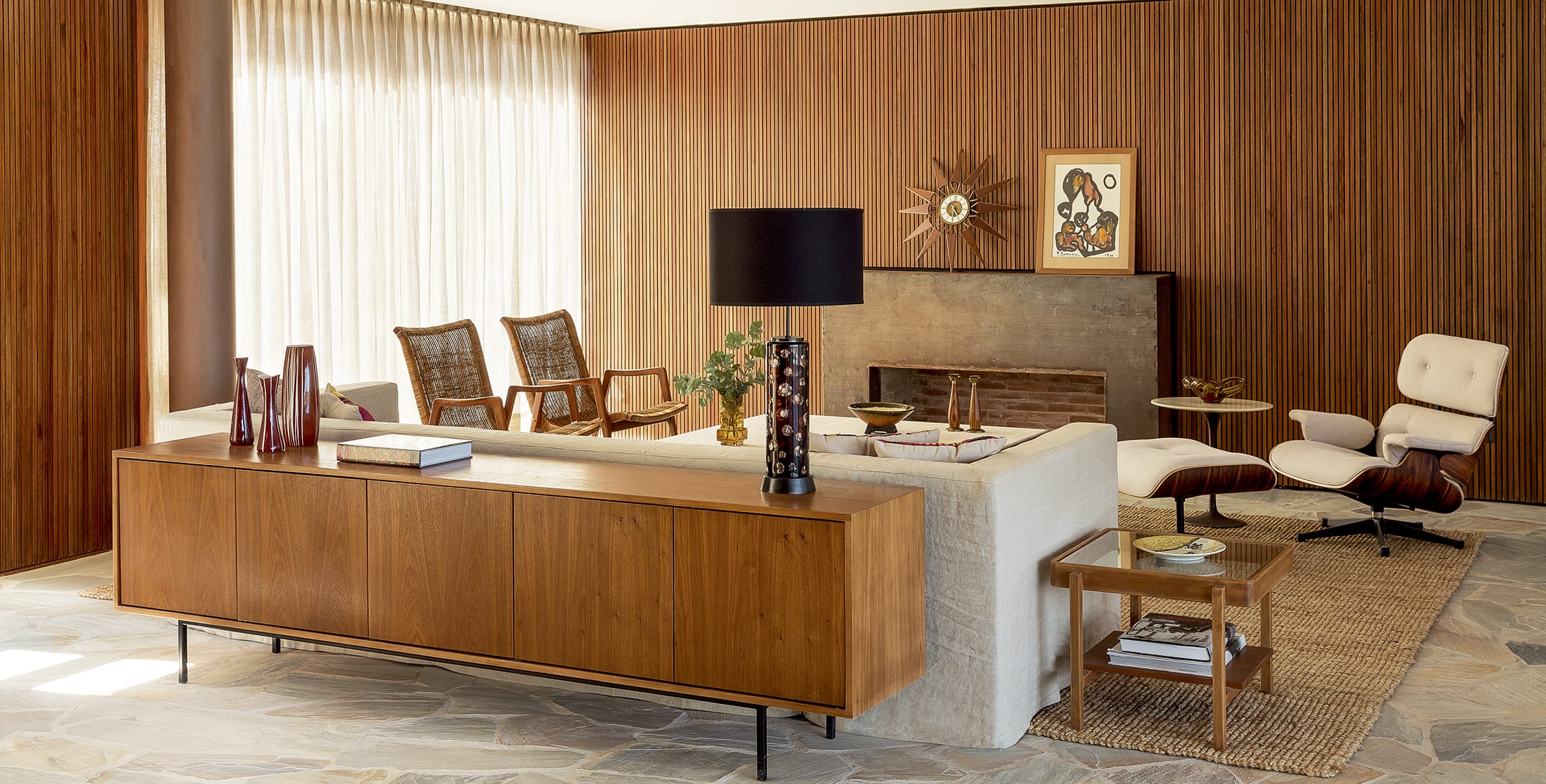 Mid-century modern living room with wooden panels, stylish furniture, brown sideboard, and an Eames lounge chair.