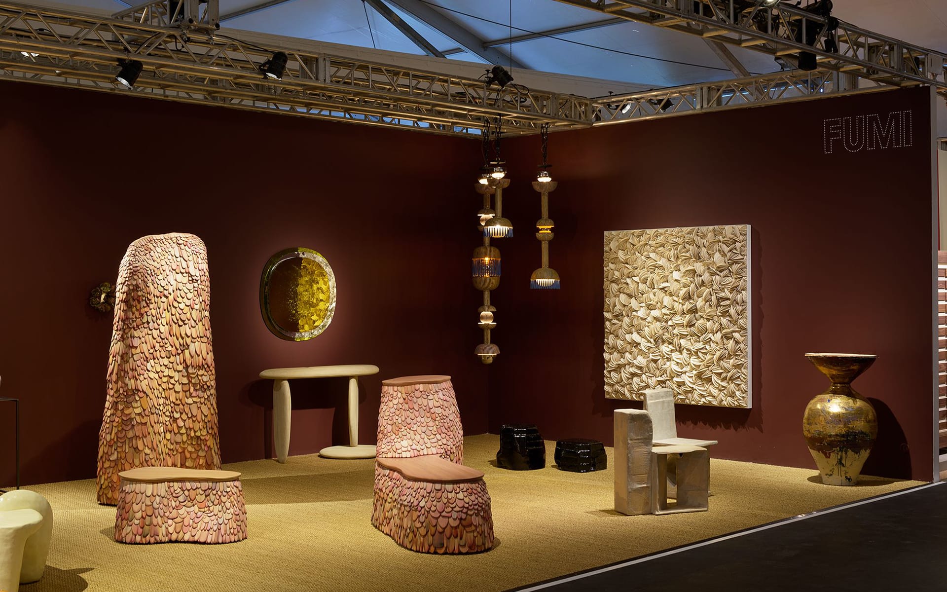 Art gallery booth with abstract wooden furniture, sculptures, and wall art in a warmly lit exhibition space.