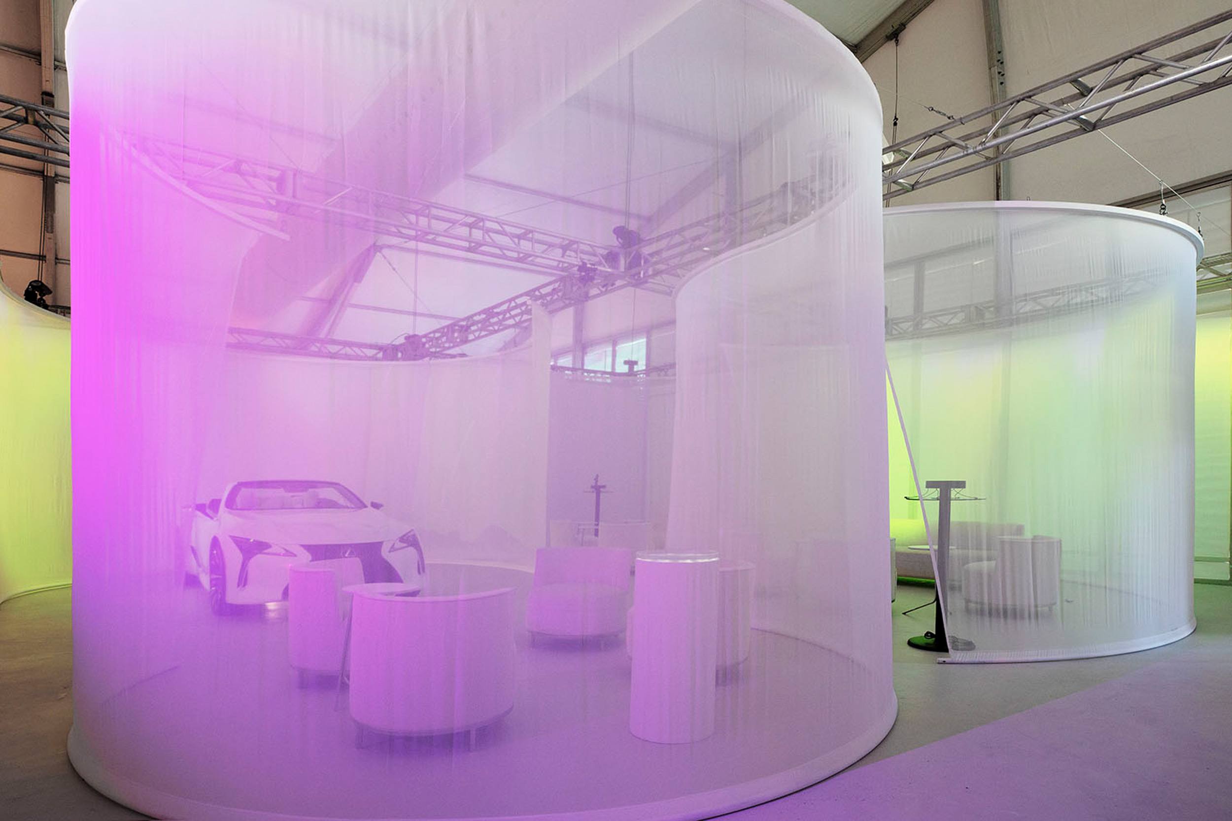Futuristic exhibit with a car surrounded by transparent purple drapes and modern furniture, creating a vibrant atmosphere.