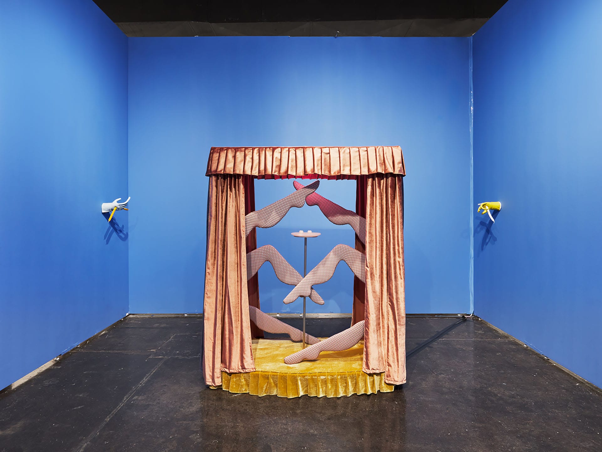 Art installation of mannequin legs in patterned stockings, positioned in a small curtained booth against vibrant blue walls.