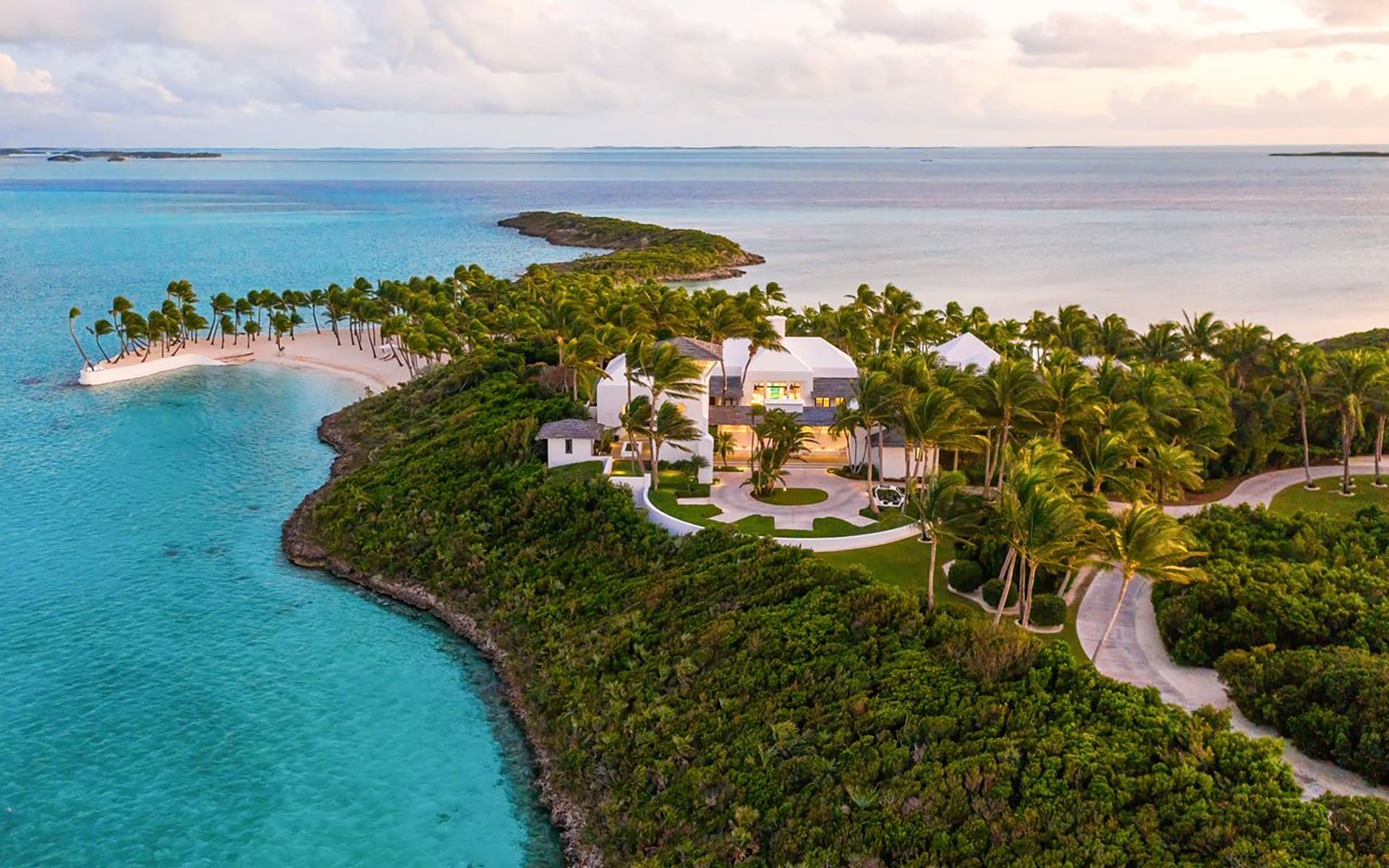 Aerial view of a tropical island with lush greenery, sandy beaches, and turquoise waters under a cloudy sky.