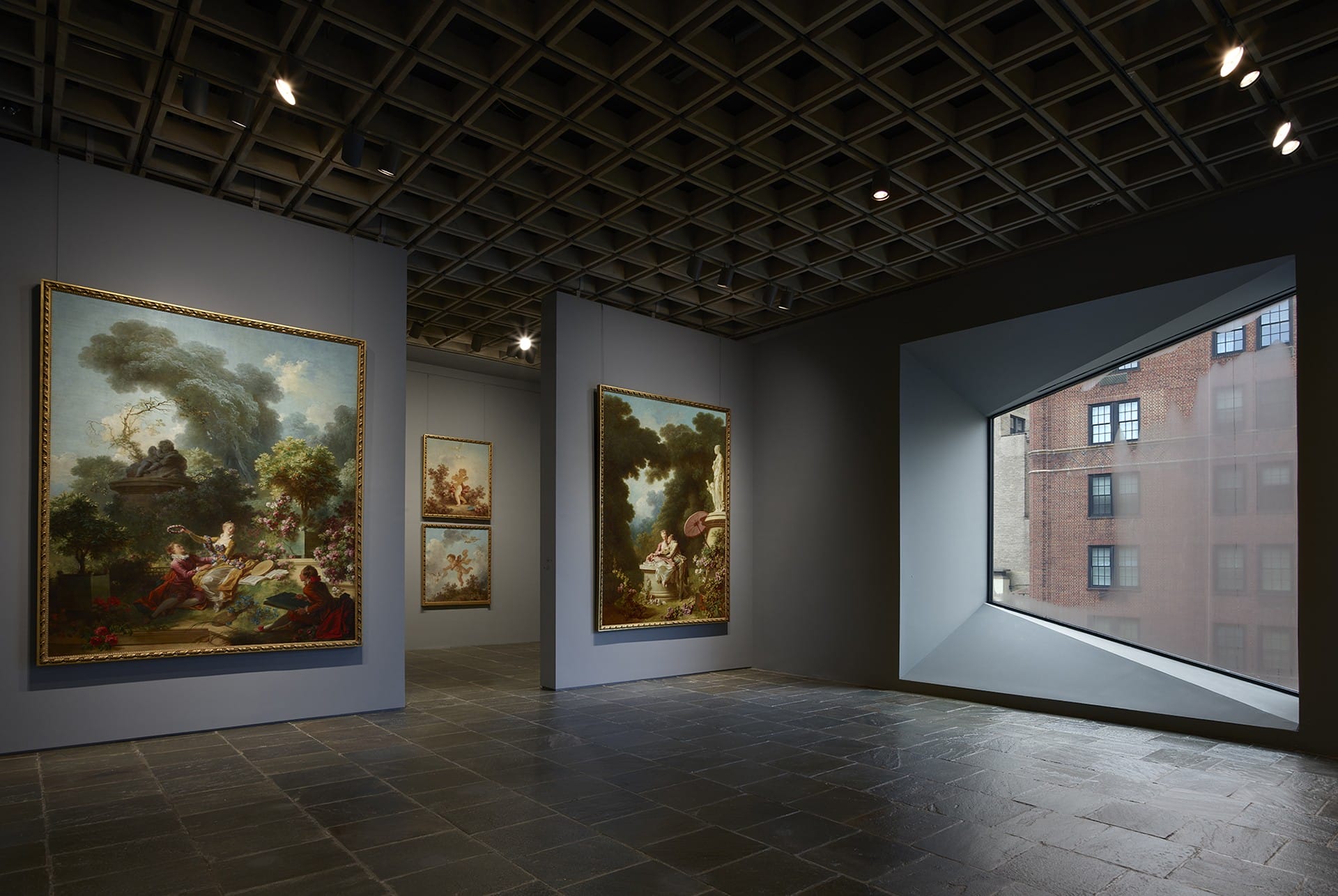 Art exhibit with classic paintings in a modern gallery, featuring a large window with a view of an urban brick building exterior.