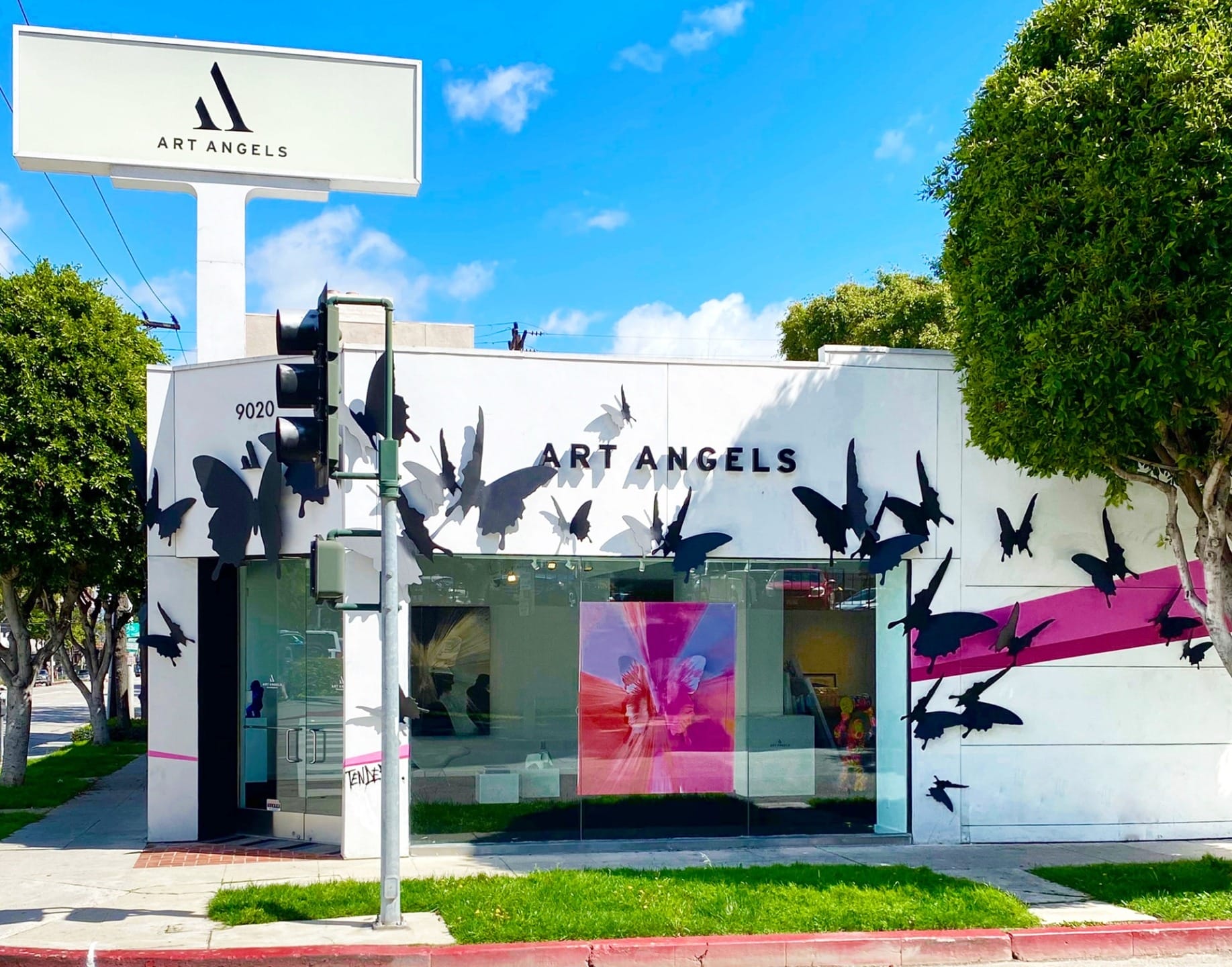 Art Angels gallery exterior with butterfly mural, located at a street corner with trees and clear blue sky in the background.