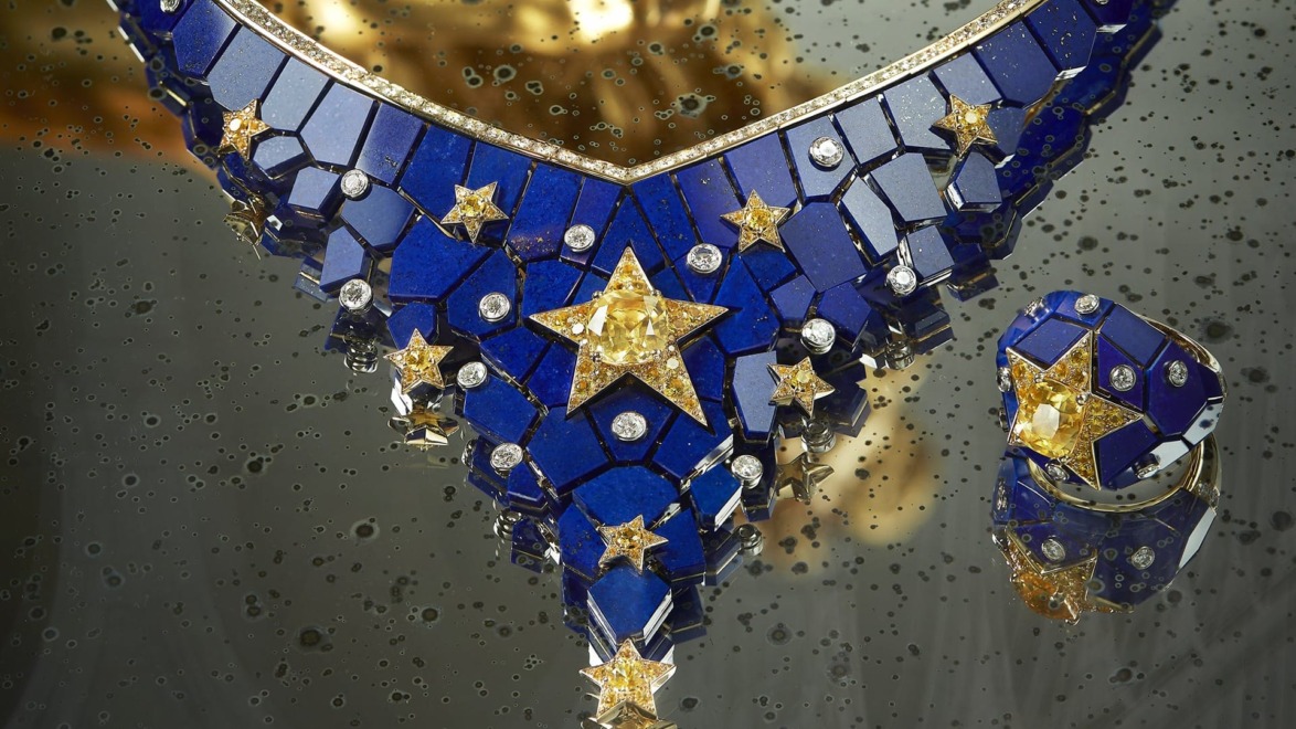 Intricate blue and gold jewelry set with star designs on a reflective surface with water droplets.