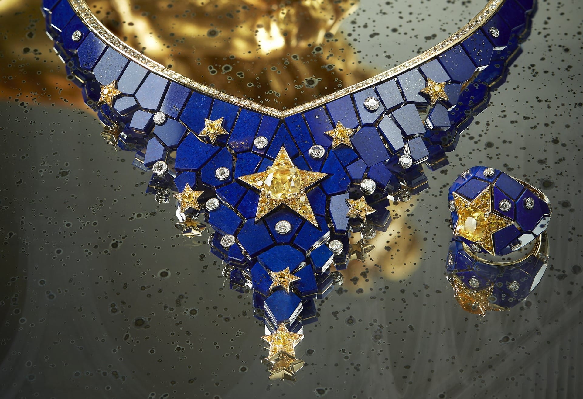 Intricate blue and gold jewelry set with star designs on a reflective surface with water droplets.