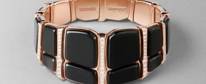 Hermès bracelet with black ceramic tiles, rose gold accents, and embedded diamonds on a gray background.