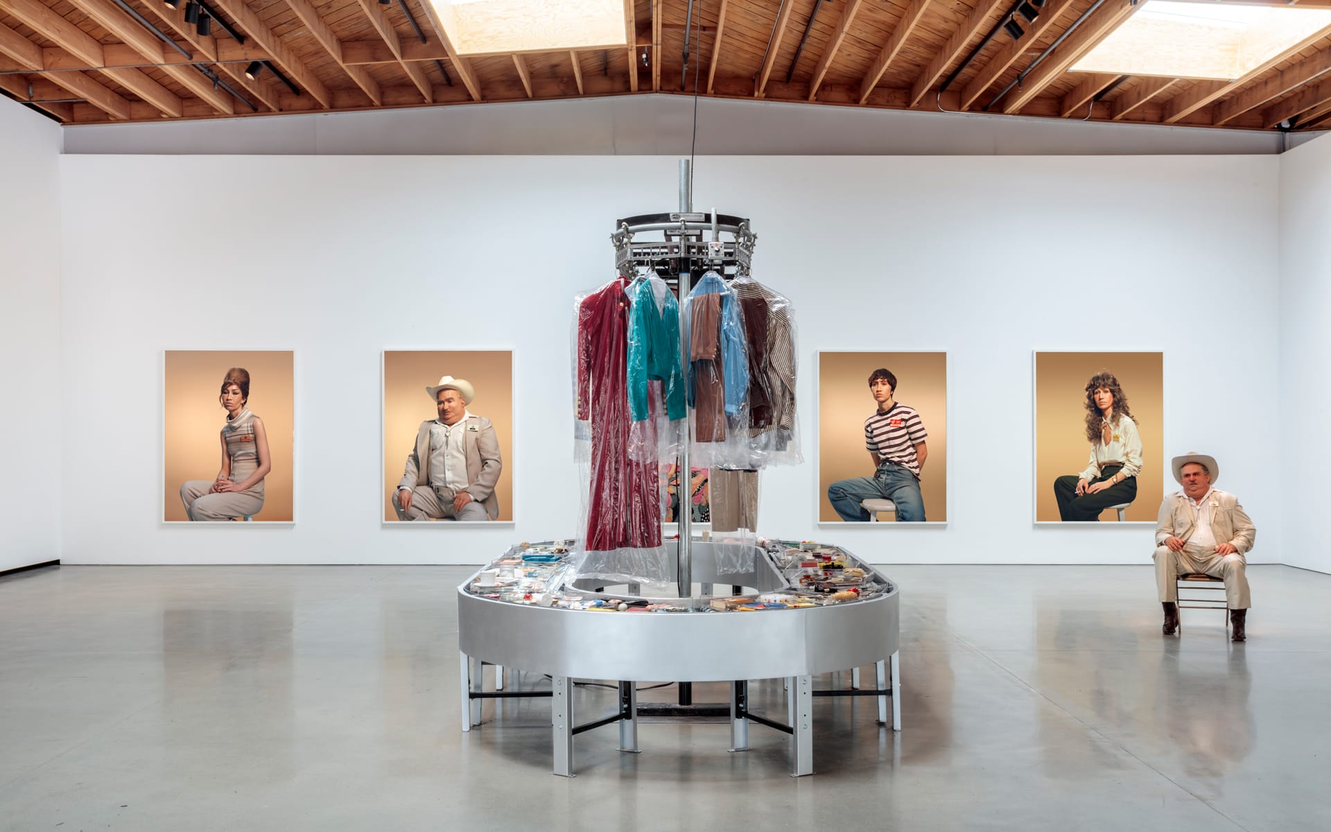 Art gallery with portraits on the walls and a rotating rack showcasing clothing in the center of the room.