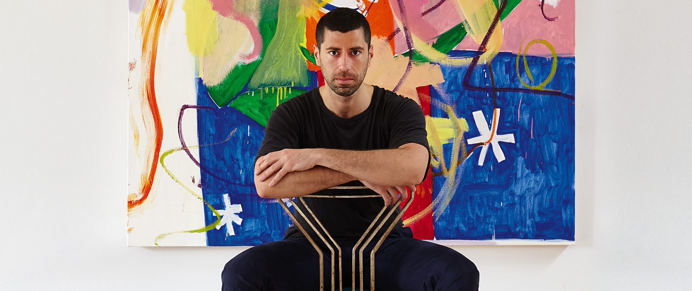 Man sitting on a chair in front of a colorful abstract painting.