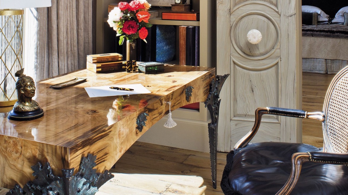 Elegant wooden desk with a floral arrangement, books, and a bust decoration in a stylish room with a unique door design.