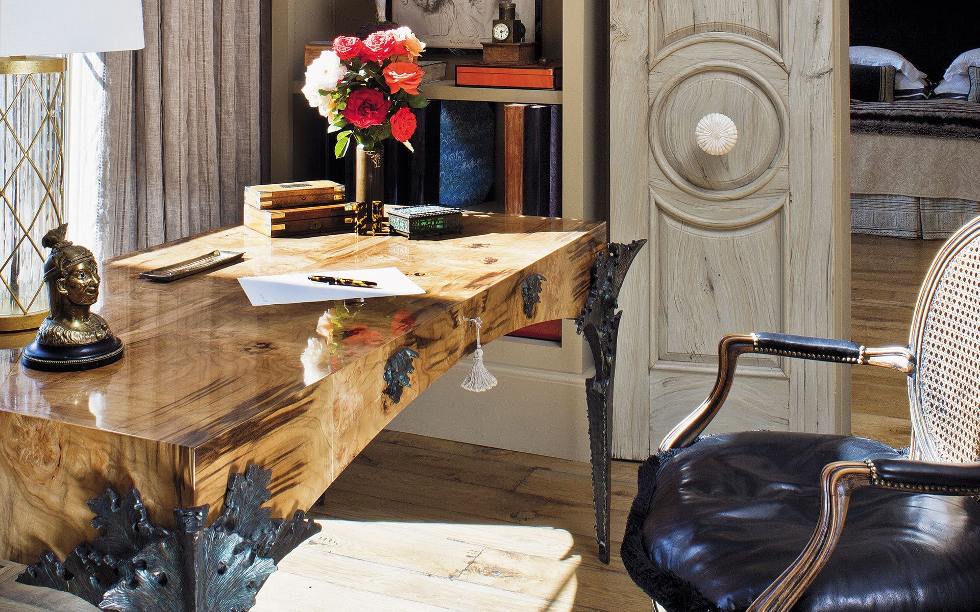 Elegant wooden desk with a floral arrangement, books, and a bust decoration in a stylish room with a unique door design.