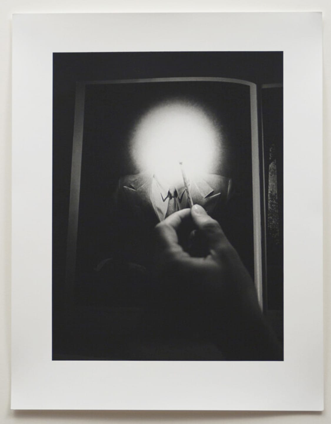Hand holding a lit match in front of a blurred face on a black and white photograph.