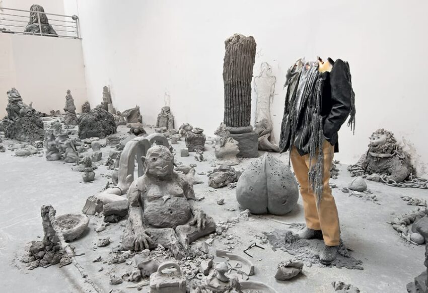 Art installation featuring abstract sculptures and a headless figure in a gallery space with concrete flooring.