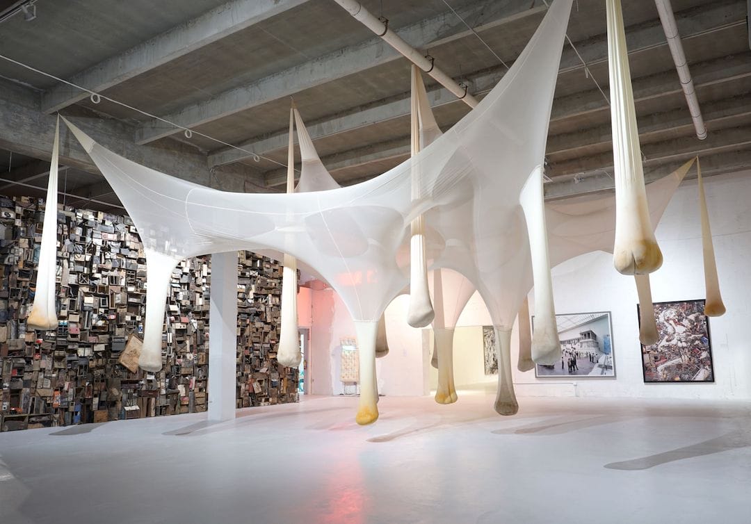 Art installation with large, stretched fabric structures hanging from the ceiling in a spacious gallery setting.